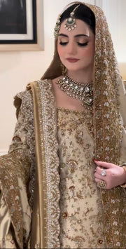 Haris Shakeel Mahrani ivory-gold bridal ensemble featuring a long heavily embellished shirt with intricate handwork including zardozi, dabka, naqshi, and delicate sequin detailing forming graceful floral and traditional motifs, paired with a magnificently worked dupatta with dense borders and finely finished edges, perfect for bridal wear with statement jewelry and traditional headpiece.