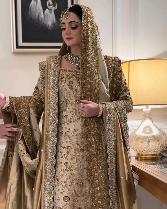 Haris Shakeel Mahrani ivory-gold bridal ensemble featuring a long heavily embellished shirt with intricate handwork including zardozi, dabka, naqshi, and delicate sequin detailing forming graceful floral and traditional motifs, paired with a magnificently worked dupatta with dense borders and finely finished edges, perfect for bridal wear with statement jewelry and traditional headpiece.