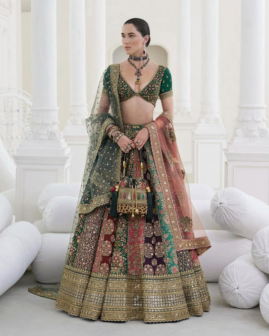 Sabya Sachi Mukherjee multi-color bridal lehenga choli featuring a deep emerald green embellished choli paired with a richly crafted lehenga showcasing intricate gold embroidery and panelled patterns in maroon, purple, pink, and green hues, with a heavily adorned lehenga border detailed in fine zari, sequins, and handcrafted embellishments, completed with a sheer embellished dupatta with gold detailing, perfect for barat, reception, walima, and grand festive occasions.
